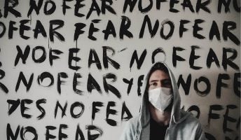 man wearing face mask in front of wall with the words no fear