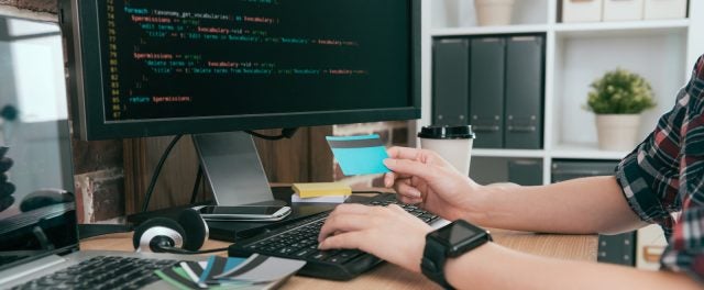 The arms of a Web Designer at a desk, coding a website on a desktop computer, using a keyboard and script program